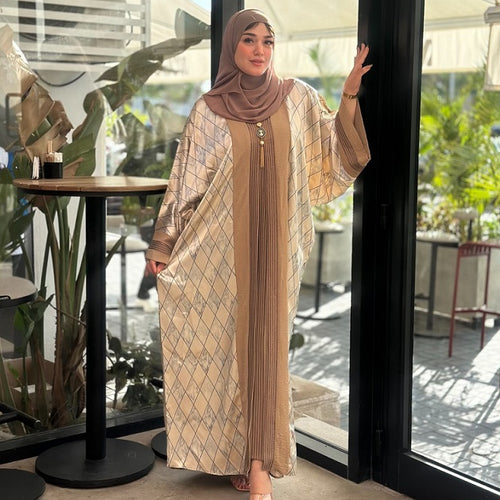 Woman in a patterned abaya standing in a modern indoor setting with plants.