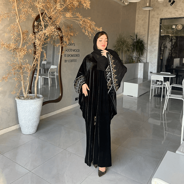 Woman in a black outfit with a patterned hood standing in a modern indoor setting.