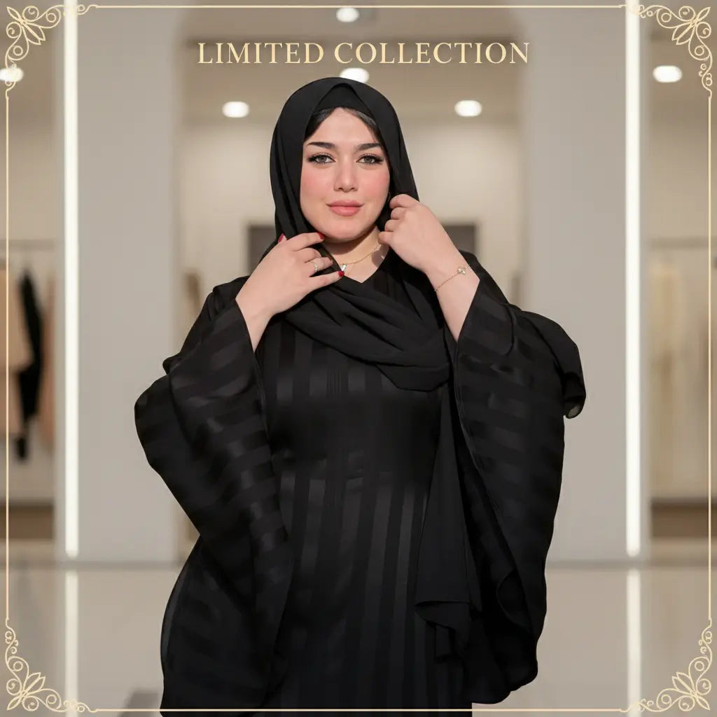 Woman wearing a black abaya in an outdoor setting with greenery and a red wall.