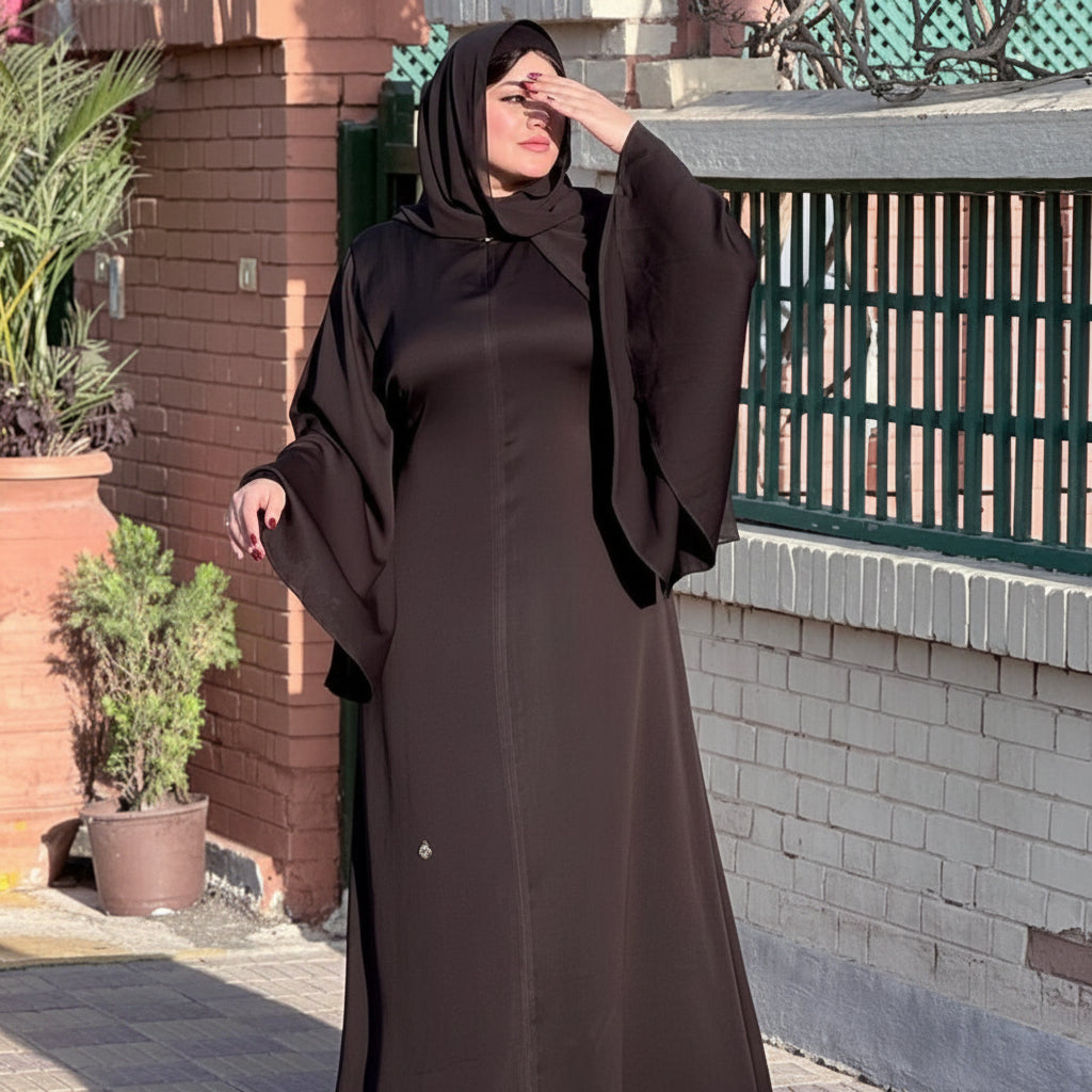 Woman wearing a long dark brown abaya outdoors near a building.